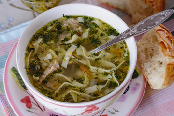 Noodle soup in a deep plate is on the dining table next to bread sticks 