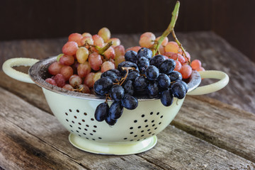 Bunches of pink and black grapes lie in a colander on old wooden boards