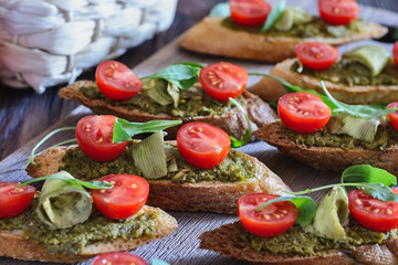 Toasts with pesto sauce, cherry tomatoes, avocado chips and leaves of arugula on a wooden table ready for eating
