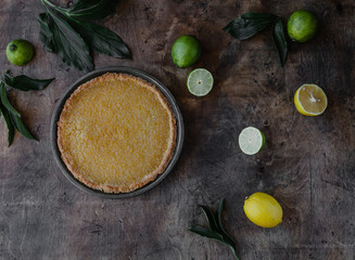 top view of tasty lemon pie and limes with lemons on wooden table