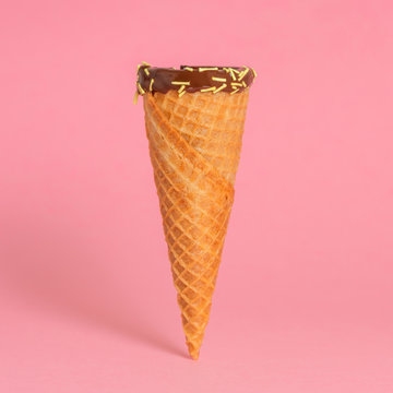 funny creative concept of close up empty wafer cone with chocolate glaze and colorful sprinkles over pastel pink background