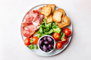 Antipasto Plate with dried bread, ham serrano, tomato cherry and purple olives. White background.