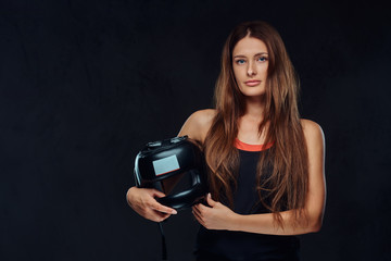 Portrait of a beautiful brunette female boxer in sportswear holds a protective helmet, looking at a camera. Isolated on dark textured background.