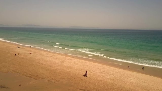 Drone footage flying over people on a long sandy beach with turquoise water