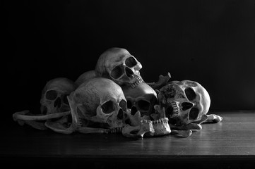 Pile of skulls and bones put on dark wooden plank which has dim light and the dark wall background