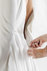 Fototapeta na wymiar Woman helps bride to put on wedding dress