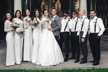 Beautiful wedding couple stands with friends before black steel gates