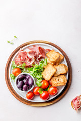 Antipasto Plate with dried bread, ham serrano, tomato cherry and purple olives. White background.