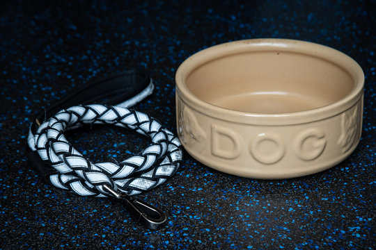 An empty large ceramic dog food bowl and lead on a dark kitchen floor