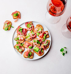 Mini open sandwiches with jamon serrano on white plate and rose wine