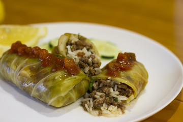 Cigar of cabbage served on white plate accompanied by slices of cucumber, sicilian lemon and tomato...