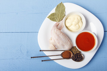Chicken wings, mayonnaise and tomato sauce with seasonings on a white plate. Top view on wooden table with copy space