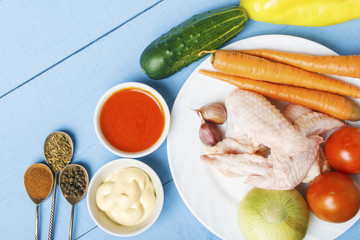Organic vegetables and uncooked chicken wings for preparation healthy food. Silver spoons with spices. Fresh tomato cauce and mayonnaise on wooden table. Top view with copy space