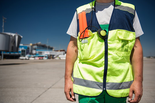 Work clothing. Close up of male torso in signaling vest. Airport terminal, runway and blue sky on blurred background