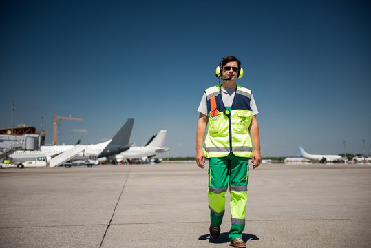 I am coming. Full length portrait of aviation marshaller walking down the runway. Man wearing sunglasses and headphones