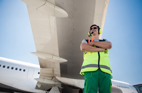 Enjoying sunny day. Low angle portrait of smiling man in sunglasses standing under airplane wing