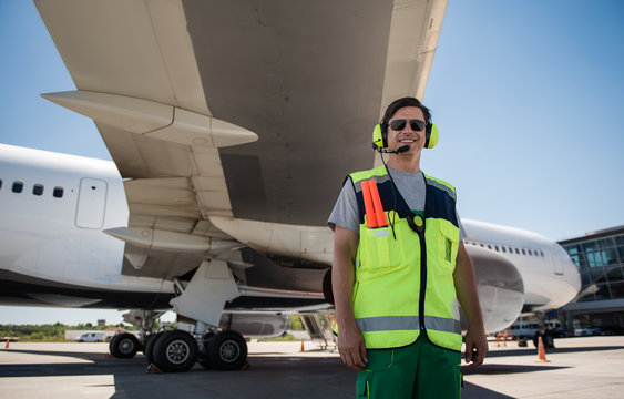 I love my job. Smiling man in sunglasses standing at airdrome. Blue sky and aircraft with open cargo door on background