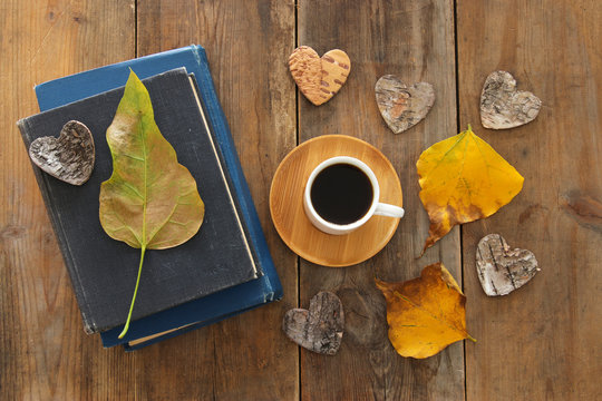 top view image of coffee cup over wooden , dry autumn leaves and stack of books.