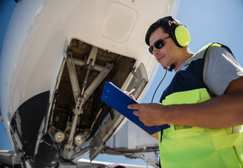 Doing paperwork. Low angle portrait of man in sunglasses filling out documents while standing near passenger plane