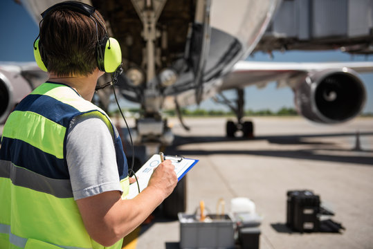 Focusing on work. Back view of ground crew member noting data on clipboard while checking aircraft before the flight