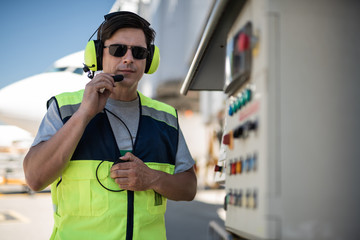 Successful job.. Serene airport worker standing near technical equipment. Man is going to talk on...