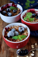 Crumble with berries in portion ceramic bowls topped with black currant and mint
