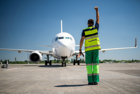 Nice to see you. Back view of aviation marshaller doing job at airport. Sky, modern aircraft and runway on background