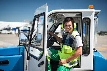 Naklejka premium Joyful day. Cheerful man posing at camera before driving. He is holding the wheel and wearing headset