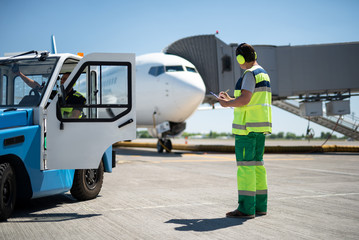 Excellent teamwork. Full length portrait of man looking at aircraft and writing information while...