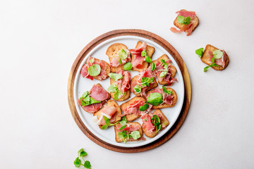 Mini open sandwiches with jamon serrano on white plate