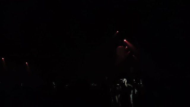 Handheld shot of light show and silhouette people dancing music in concert.