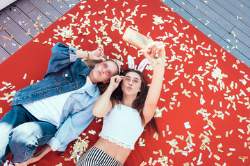 Top view portrait of satisfied women watching at mobile while taking selfie on contemporary mobile. They having leisure on comfortable couch. Positive comrades spending time together concept