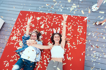 Top view portrait of happy ladies keeping hands together while lying on cozy red sofa. They...