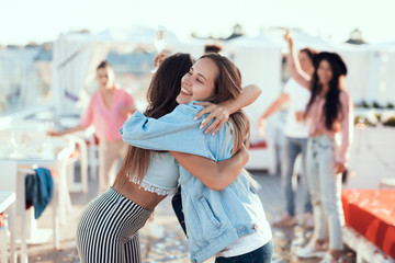 Outgoing lady hugging best friend while holding glass of beverage. Meeting of glad comrades concept
