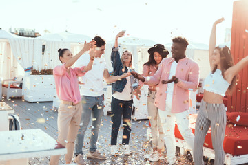 Positive females and cheerful men dancing while entertaining together outside. Glad friends during celebration concept - obrazy, fototapety, plakaty