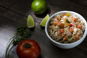 Tabule, comida libanesa tradicional, servida em uma tigela de porcelana branca acompanhada de limão e tomate sobre a mesa de madeira rústica