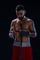 Sports boxer man pulls on the hand wrist wraps. Oriental male model isolated on black background.