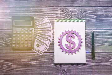 calculator, dollars, gear, notepad, pen on a wooden background. business planning.