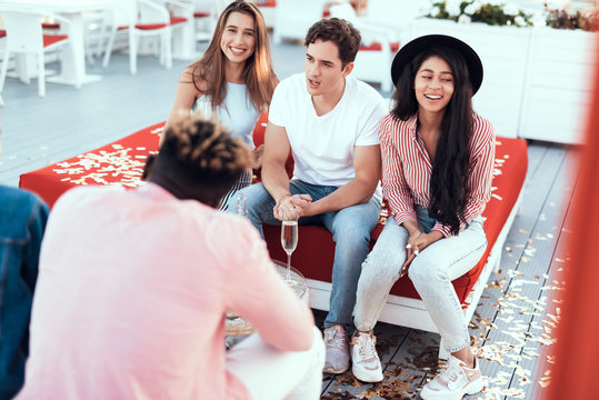 Positive male communicating with beaming ladies while sitting on cozy sofa outdoor