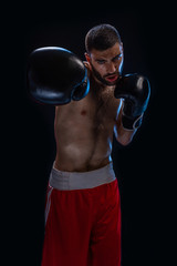 The boxer is ready to deal a powerful blow. Photo of muscular man on black background.