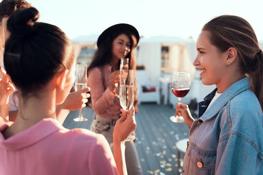 Optimistic ladies drinking alcohol liquid while talking together outside. They holding glasses in hands