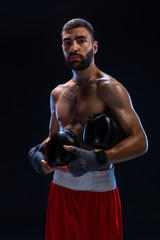 Fototapeta na wymiar Handsome athletic guy in a red shorts on a black background. The boxer is fetching his breath after practicing hooks and blows.