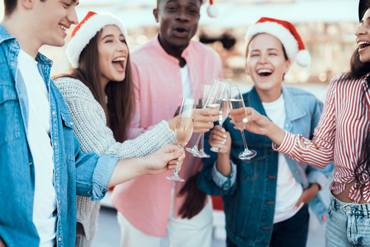 Laughing girls and beaming men speaking while drinking glasses of champagne. They wearing red hats during new year celebration