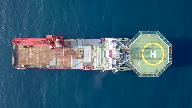 Aerial footage of a Medium size red Offshore supply ship with a Helipad and a large crane