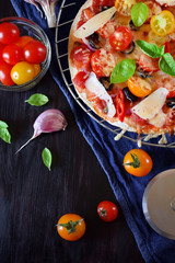 Pizza with cherry tomatoes, tomato sauce, cheese and basil leaves against the dark background. Mediterranean cuisine meal