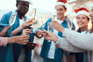 Positive males and cheerful girls keeping bengal lights while tasting alcohol liquid during new year celebration