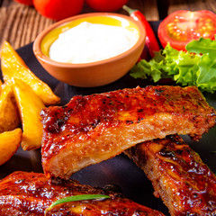 bbq spareribs on the plate with green salad and white sauce.