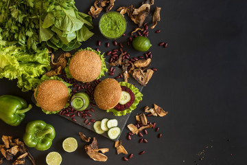 Vegan burgers with beet cutlet and green smoothies on black background. Healthy vegan food. Detox diet. Flat lay with copy space.