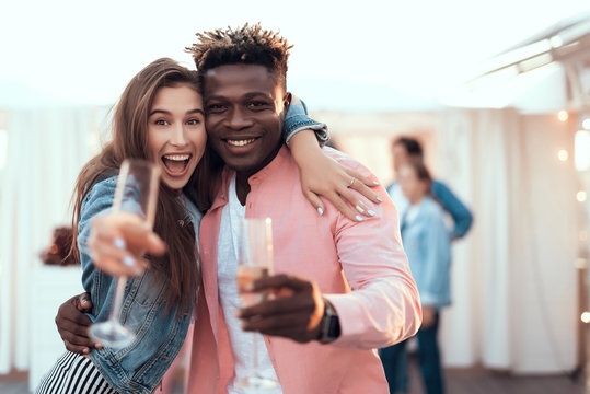 Portrait of laughing girl and smiling male embracing while tasting alcohol beverage. Glad female gesticulating hand. They looking at camera