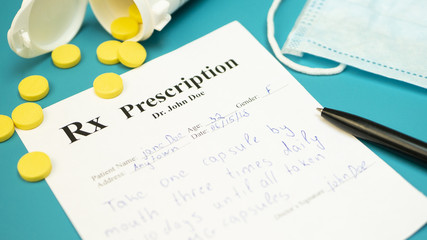 Prescription for tablet pills or drugs on blue green background with bottle and yellow tablets or pills and medical mask